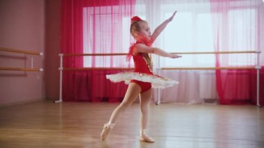 Kırmızı elbiseli küçük bir kız bale hareketleri sergiliyor.