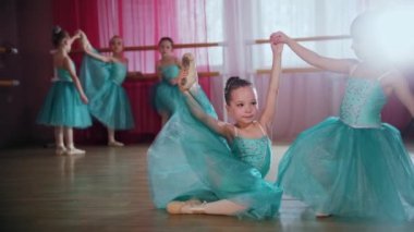 Mavi elbiseli küçük kızlar çemberin içinde oturur ve gerinirler.