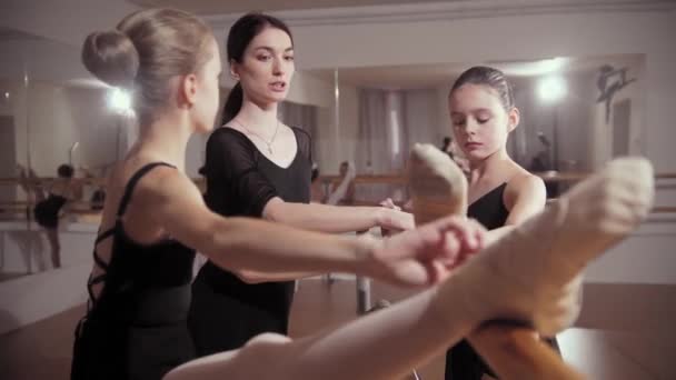 Balletttraining - Ballerinas in schwarzen Kleidern strecken sich mit Hilfe ihres Trainers am Stand — Stockvideo