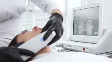 Vücut masajı - genç bir kadın yüzüne elektrikli masaj yaptırıyor. Arka plandaki hareketlerini gösteren bir monitörle.