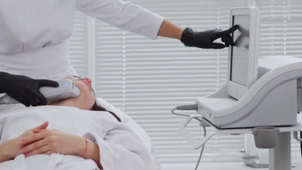 Vücut masajı - genç bir kadının yüzüne elektrik masaj yapılıyor ve terapist monitörü işaret ediyor. — Stok video
