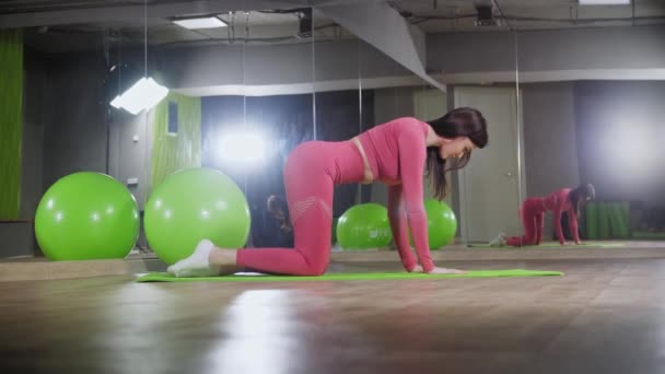 Pembe kostümlü genç kadın yoga minderinde egzersiz yapıyor. — Stok video