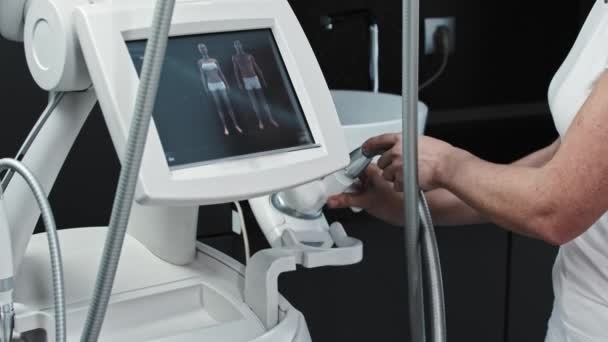 De therapeut neemt een elektrisch apparaat voor massage en selecteert de functie op de monitor — Stockvideo