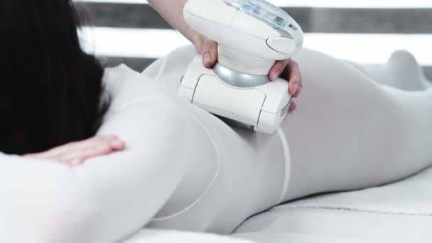 Молодая женщина с черными волосами получает электрический массаж на теле в специальном белом костюме — стоковое видео