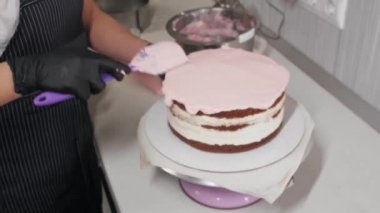 Pasta şefi pastanın üzerine pembe krema sürüyor.