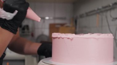 Büyük bir spatula kullanarak pastanın kenarını pembe kremayla yumuşatıyor.