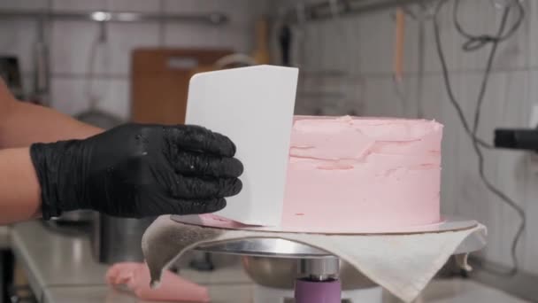 Verzacht de zijkant van de taart met roze crème met behulp van een grote spatel — Stockvideo