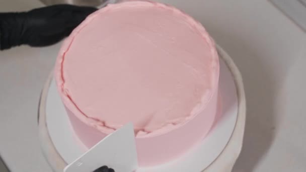 A cukrász elsimítja a torta oldalát rózsaszín édes krémmel egy nagy spatulával — Stock videók