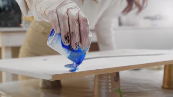 Una mujer vertiendo resina epoxi azul sobre la superficie transparente — Vídeo de stock
