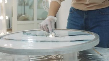 Genç bir kadın spatula kullanarak epoksi reçine sanat objesinin yüzeyini düzleştiriyor.