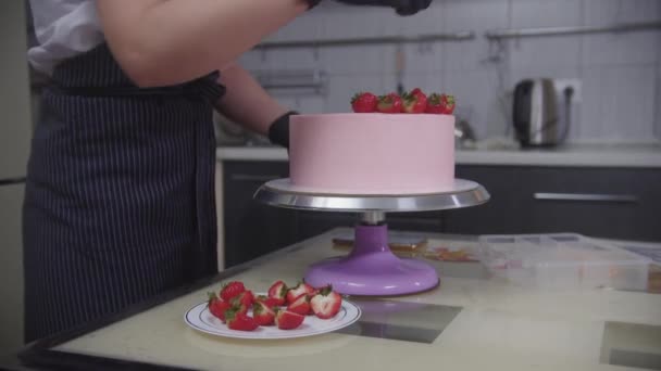 Wyroby cukiernicze - cukiernik zdobiący różowe ciasto truskawkami — Wideo stockowe