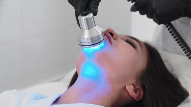 Genç esmer kadın yüz bakımı yaptırıyor. Çenesine ışık cihazı takıyor. — Stok video