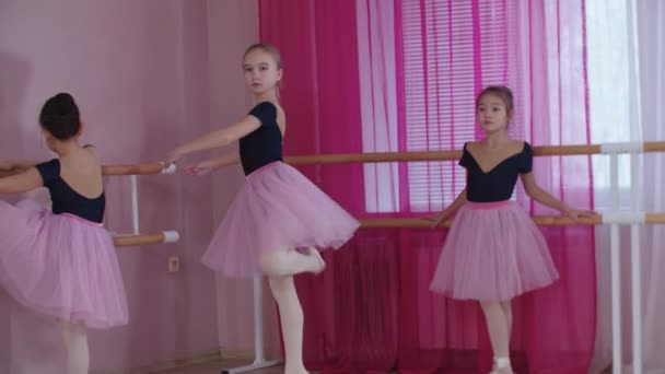 Balletttraining - drei Mädchen in schönen Kleidern trainieren im Studio und eines von ihnen beginnt zu tanzen — Stockvideo