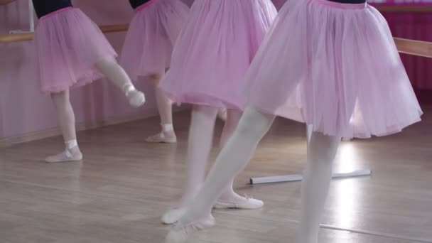 Ballet training - five girls in beautiful dresses training and stretching their legs by the stands in the studio — Stock Video