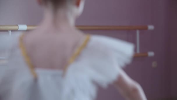 バレエのトレーニング-スタジオで実行されている白いドレスの少女とバレエの動きを示すスポットでジャンプ-カメラを見て — ストック動画