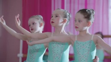 Bale eğitimi. Mavi elbiseli üç balerin kız tribünde durup hareketlerini eğitiyor.