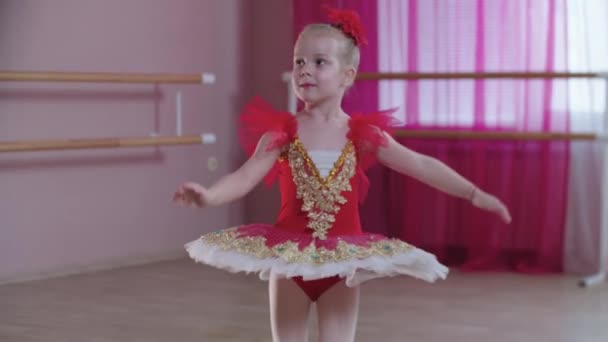 Тренировка балета - маленькая серьезная девушка в красном платье, стоящая в балетном положении и прыгающая на месте — стоковое видео