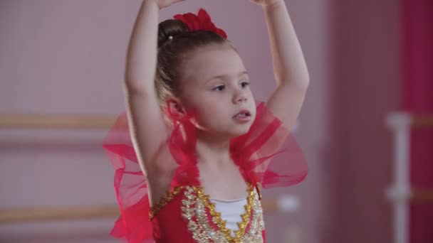 Trening baletowy - dziewczynka w czerwonej sukience stojąca w pozycji baletowej i powoli kręcąca się w kółku — Wideo stockowe