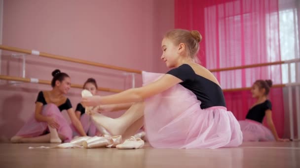 Pięć baletnic w pięknych sukienkach siedzących na podłodze i jedna z nich zmieniająca swoje szpiczaste buty — Wideo stockowe