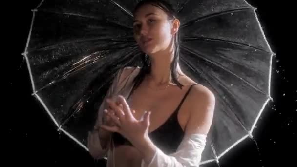 Seksi vücutlu genç bir kadın yağmurun altında durur ve şemsiyesini çevirir. — Stok video