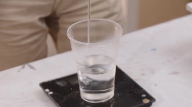 Sanatçı, plastik bir bardaktaki epoksi reçinesinin şeffaf tabanını tartır.