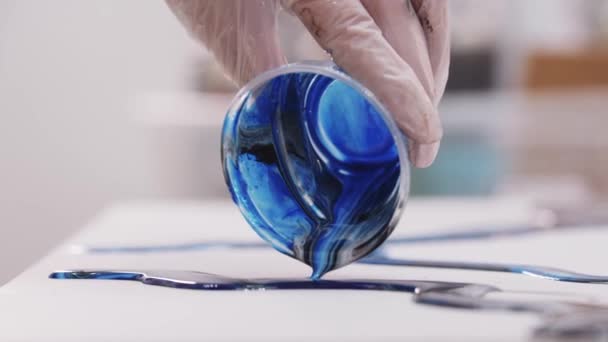 Umělec nalévá přebytek směsi hluboké modré a černé epoxidové pryskyřice na plátno — Stock video