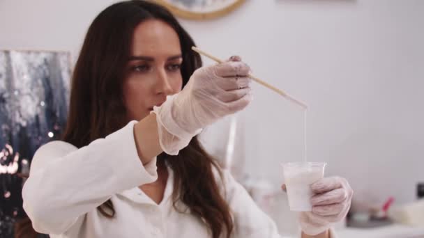 Mujer artista mezclando resina epoxi blanca en la taza de plástico — Vídeo de stock