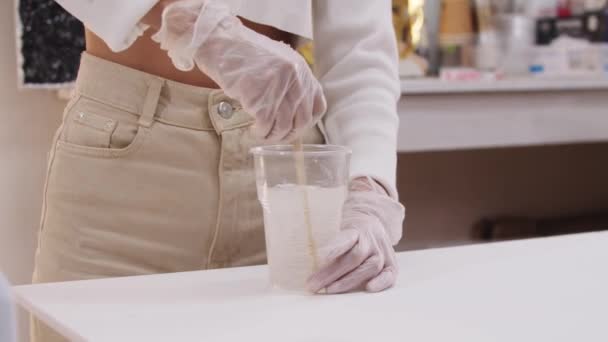 Kunstenaar kneedt een transparante basis van epoxyhars in een grote plastic beker met stokjes — Stockvideo