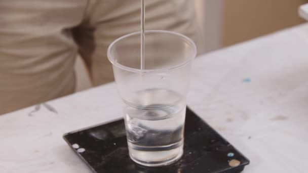 Der Künstler wiegt den transparenten Boden aus Epoxidharz in einem Plastikbecher — Stockvideo
