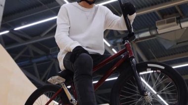 BMX sporları. Genç adam bisikletiyle sıçrama tahtasının tepesine oturur ve kameraya bakar.