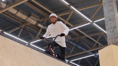 BMX spor. Genç adam bisiklete biner ve kameraya bakar. Sonra da sıçrama tahtasından aşağı atlar.