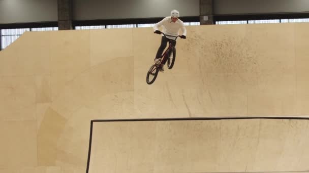 Joven montando en las rampas de madera contrachapada en su bicicleta deportiva y realizando trucos en el aire — Vídeos de Stock