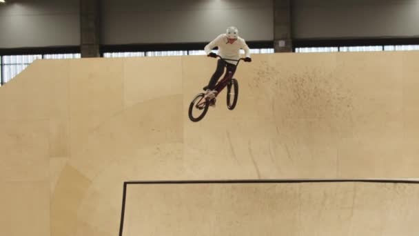 Um homem montando nas rampas de madeira compensada em sua bicicleta esportiva e realizando truques no ar — Vídeo de Stock