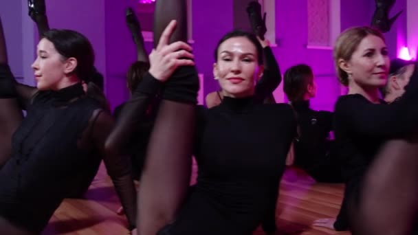 Grupp sexiga kvinnor i svarta kläder sitter i en cirkel och håller upp benet — Stockvideo