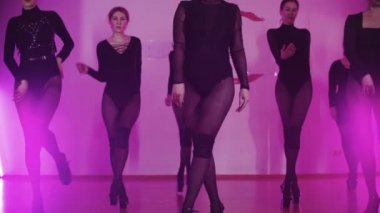 Siyah elbiseli bir grup seksi zayıf kadın senkronize olarak ilerliyorlar.