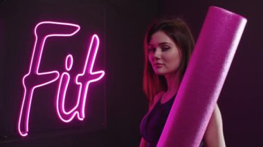 Spor kıyafetli genç bir kadın neon ışığa doğru yürür ve 