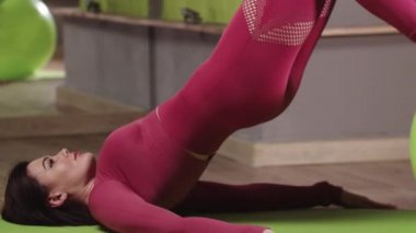 Beden eğitimi. Pembe kostümlü genç bir kadın. Ayaklarını spor topuna dayayıp egzersiz yapıyor.