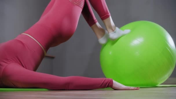 Mladá žena v růžovém kostýmu opírá nohy o fitness míč a dělá cvičení — Stock video
