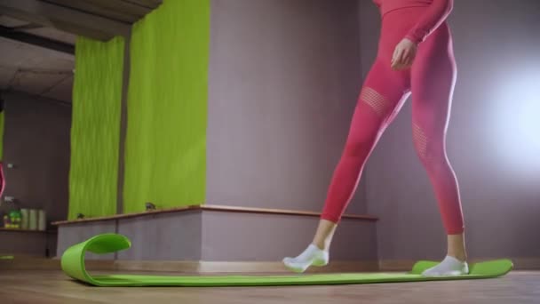 Ung kvinna i rosa kostym sätter sig på yogamattan — Stockvideo