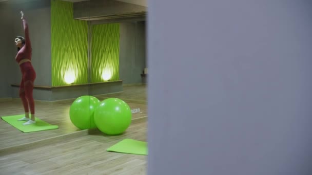 Mladá žena v růžovém kostýmu cvičení v zrcadlové fitness hale — Stock video