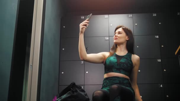 Młoda, ładna, sportowa kobieta robi sobie selfie telefonem w szatni — Wideo stockowe