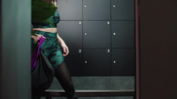 Joven mujer bonita en traje deportivo camina en el vestuario y toma una taza de plástico de su bolso — Vídeo de stock