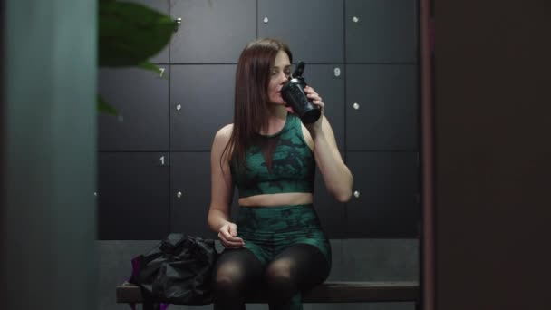 Jovem mulher bonita bebe água do copo de plástico sentado no vestiário — Vídeo de Stock