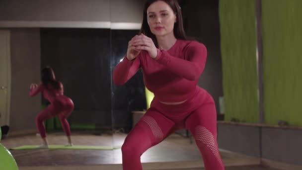 Entrenamiento de fitness - mujer joven en traje rosa haciendo sentadillas en el salón de fitness espejo — Vídeos de Stock