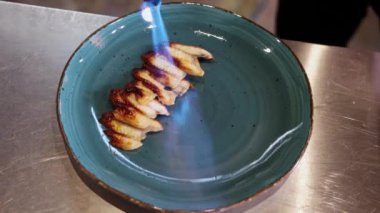 Şef balık dilimlerini tabakta yakar.