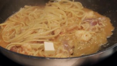 Şef kızarmış tavada domuz pastırmalı spagetti pişiriyor.