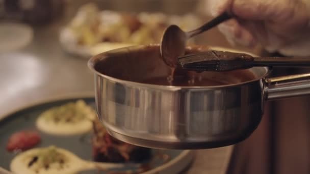 Cocina del restaurante - chef vierte la salsa de salsa salsa de la cacerola sobre el plato servido — Vídeos de Stock