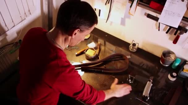 Krejčí dělá opasek a otírá kožené zbytky ze stolu — Stock video