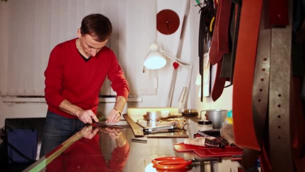 Kožená dílna - muž ostříhá hrany kusu kůže ostrým nástrojem — Stock video