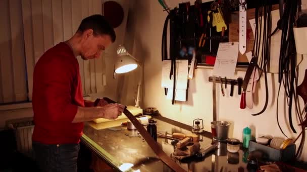 Bőrműhely - egy férfi vakot fest egy bőrövre — Stock videók